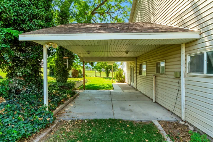 Covered outdoor concrete patio area featuring integrated lighting, vinyl siding exterior, and established green landscaping