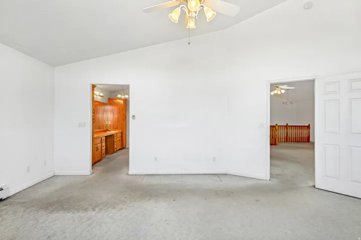 Vaulted ceiling with a ceiling fan light fixture, light carpeting, and a built-in wood vanity with cabinetry and lighting