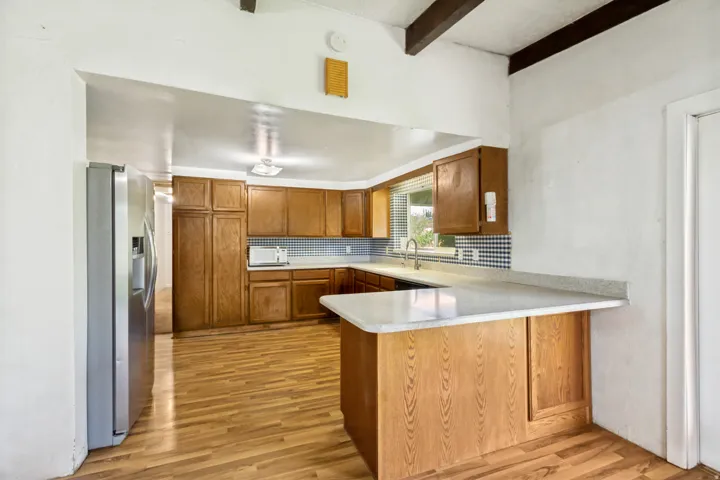 Kitchen featuring wood-finish flooring, wood cabinetry, light countertops, and a blue and white patterned tile backsplash