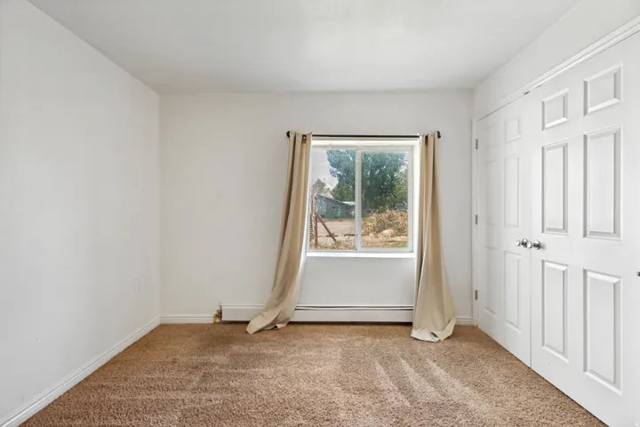 Bedroom featuring light brown carpet, white walls, and a window with a curtain rod