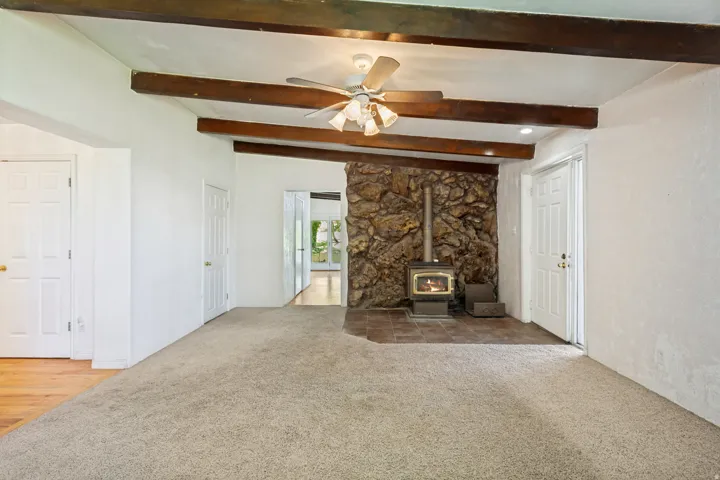 Living area featuring a stone accent wall, wood-burning stove, and exposed wood beams