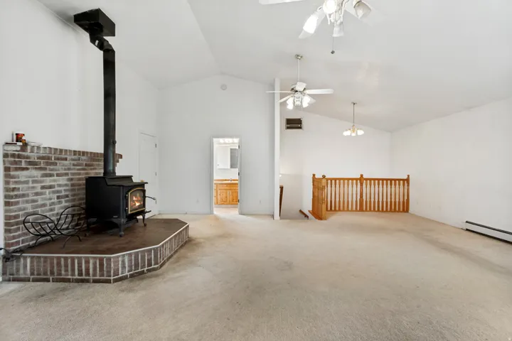 Vaulted ceilings with multiple ceiling fans, a wood-burning stove with a brick-clad hearth and surround, and an interior wood railing