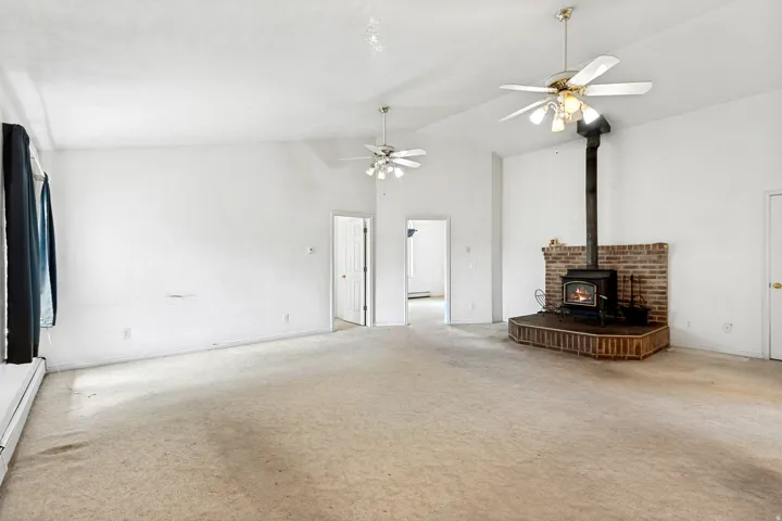 Spacious room featuring a wood-burning stove with a brick surround, light-colored carpet, and two ceiling fans