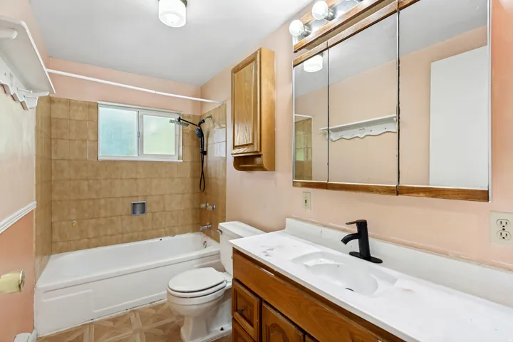 Bathroom featuring a white bathtub, a window above the tub, a vanity with an integrated sink, a dark bronze faucet, and a large medicine cabinet mirror