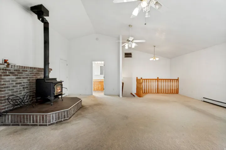 Spacious living area featuring a prominent wood-burning stove with a brick surround, vaulted ceiling, and ceiling fans
