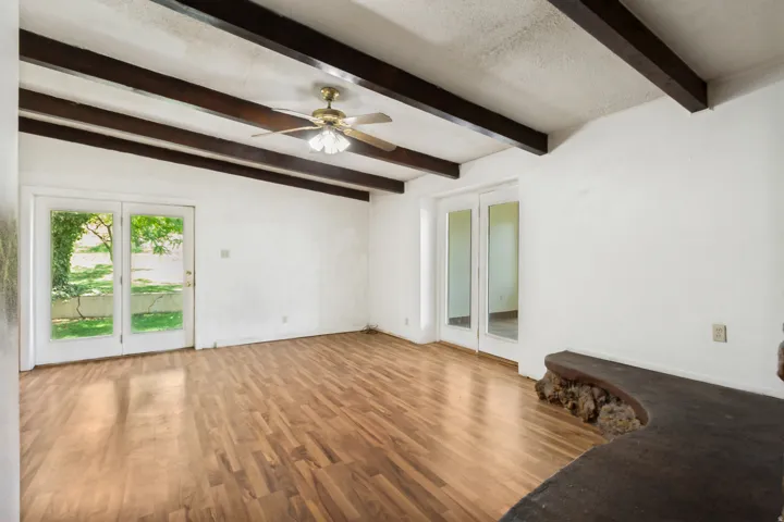 Spacious room featuring wood-finish flooring, exposed ceiling beams, and a ceiling fan