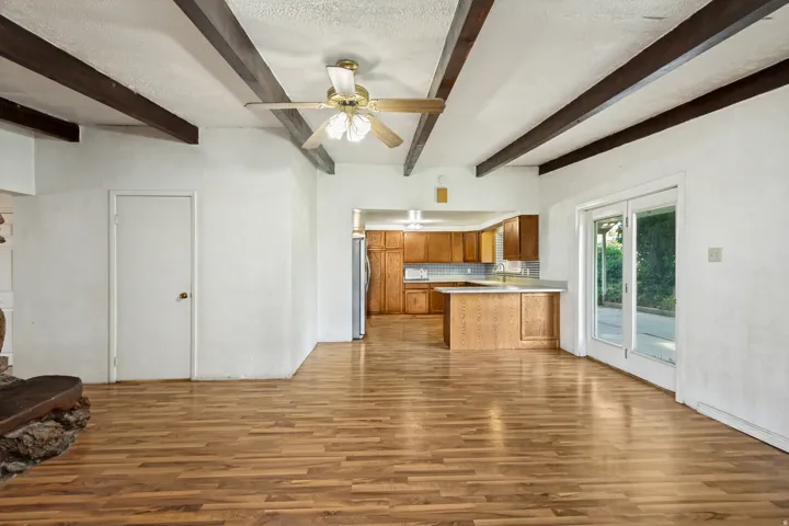 Spacious living area featuring exposed ceiling beams, wood-finish flooring, and a ceiling fan