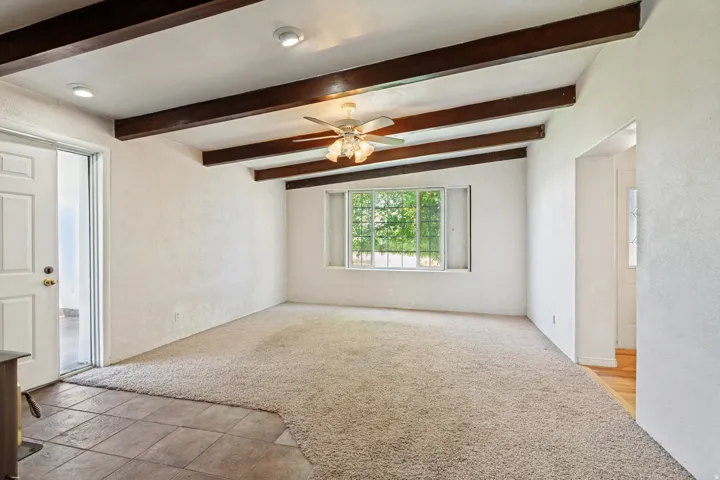 Living area featuring exposed wood-finish ceiling beams, recessed lighting, and a ceiling fan