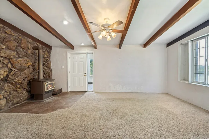 Living area featuring exposed wood ceiling beams, a stone accent wall, and a wood-burning stove with a tiled hearth