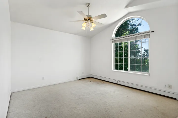 Room featuring a large arched window, vaulted ceiling, and ceiling fan with integrated lighting
