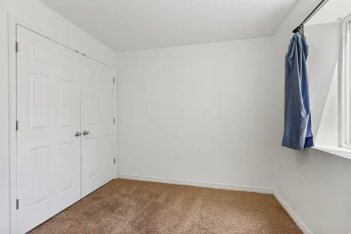 Bedroom featuring light brown carpeting, white baseboards, and a white window frame