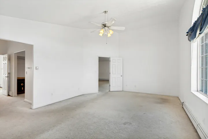 Expansive room featuring vaulted ceilings, a ceiling fan with integrated lighting, and multiple windows providing ample natural light