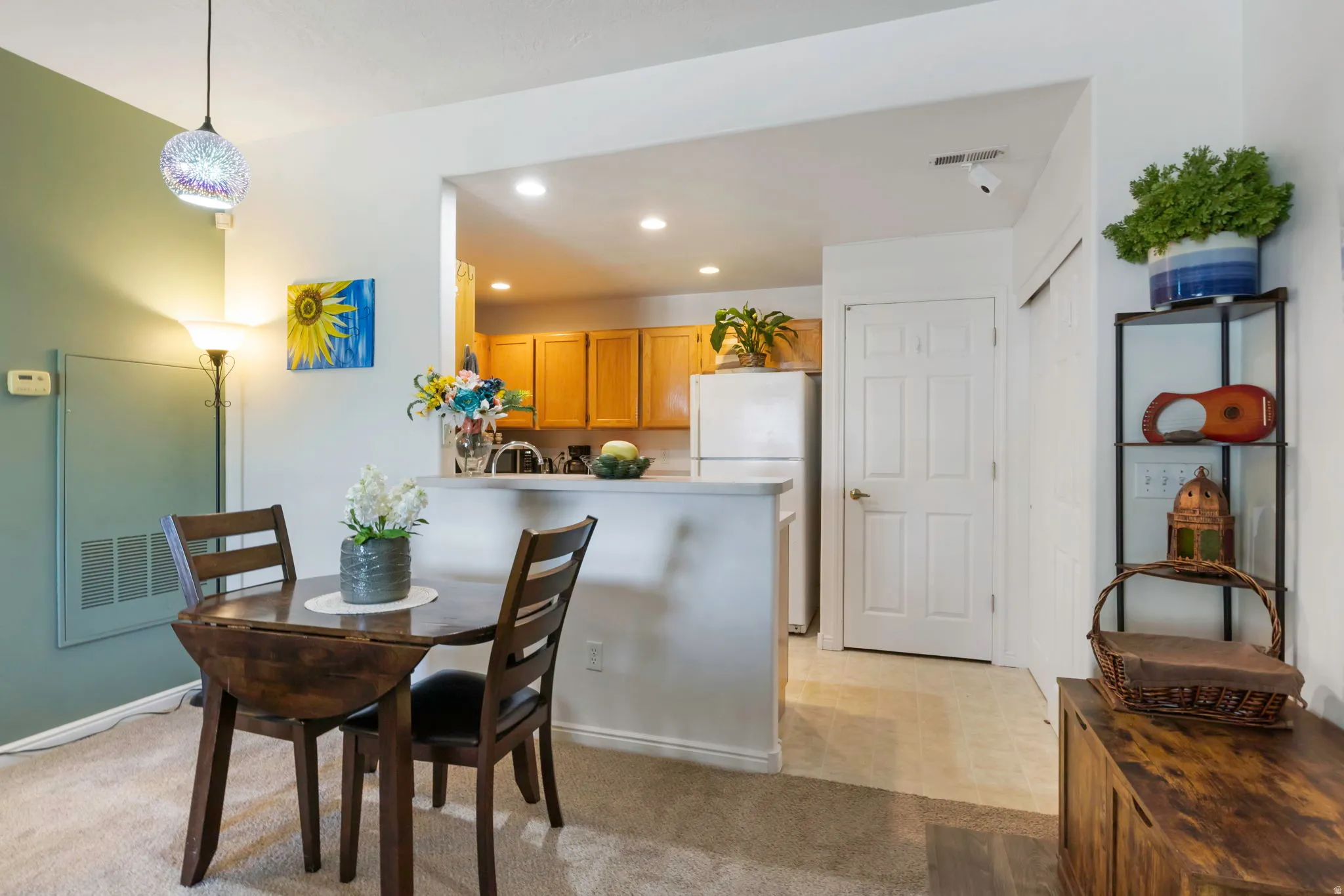 Open-concept dining space featuring textured carpeting, a stylish pendant light fixture, and a pass-through counter to the kitchen