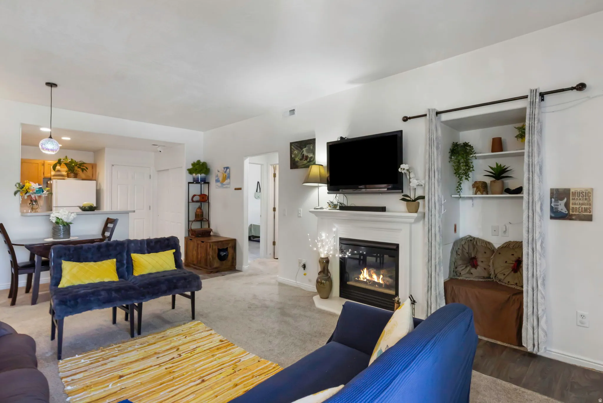 Living area featuring a fireplace with a white mantel, built-in shelving, carpeted flooring, and a dining area with a breakfast bar