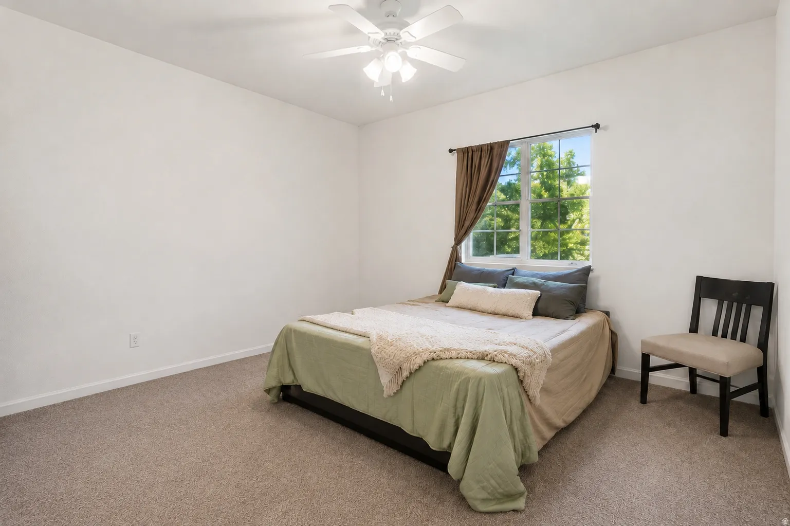 Spacious bedroom offering abundant natural light from a large window with custom drapery, ceiling fan with integrated lighting, neutral carpet flooring, and ample square footage for bedroom furnishings and layout flexibility