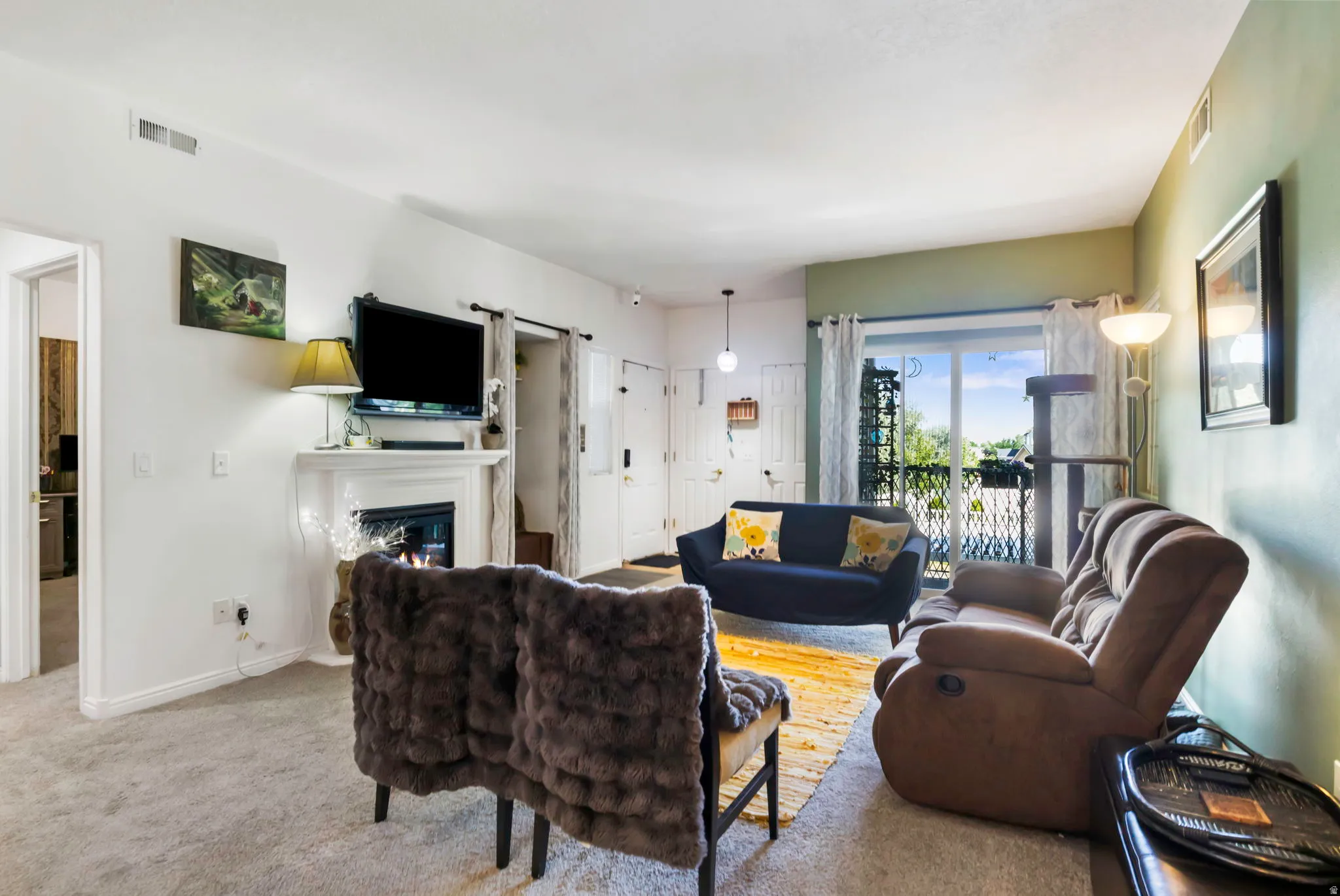 Living area featuring a fireplace with a white mantel, sliding glass doors to a balcony, and light-colored carpeting