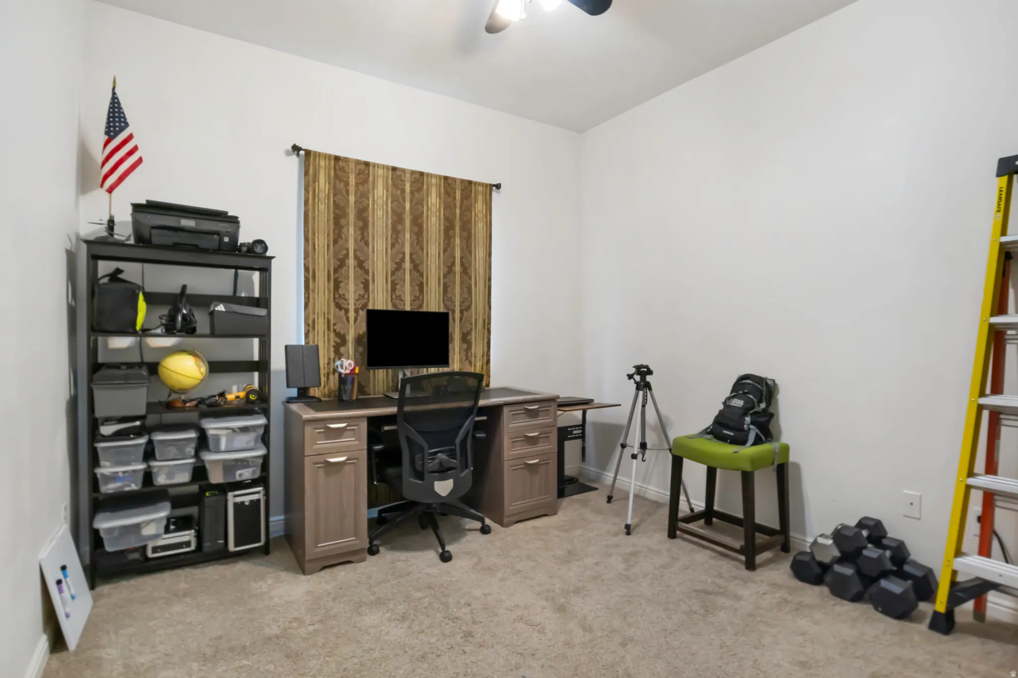 Carpeted room with a ceiling fan, window featuring patterned drapes, and neutral wall paint