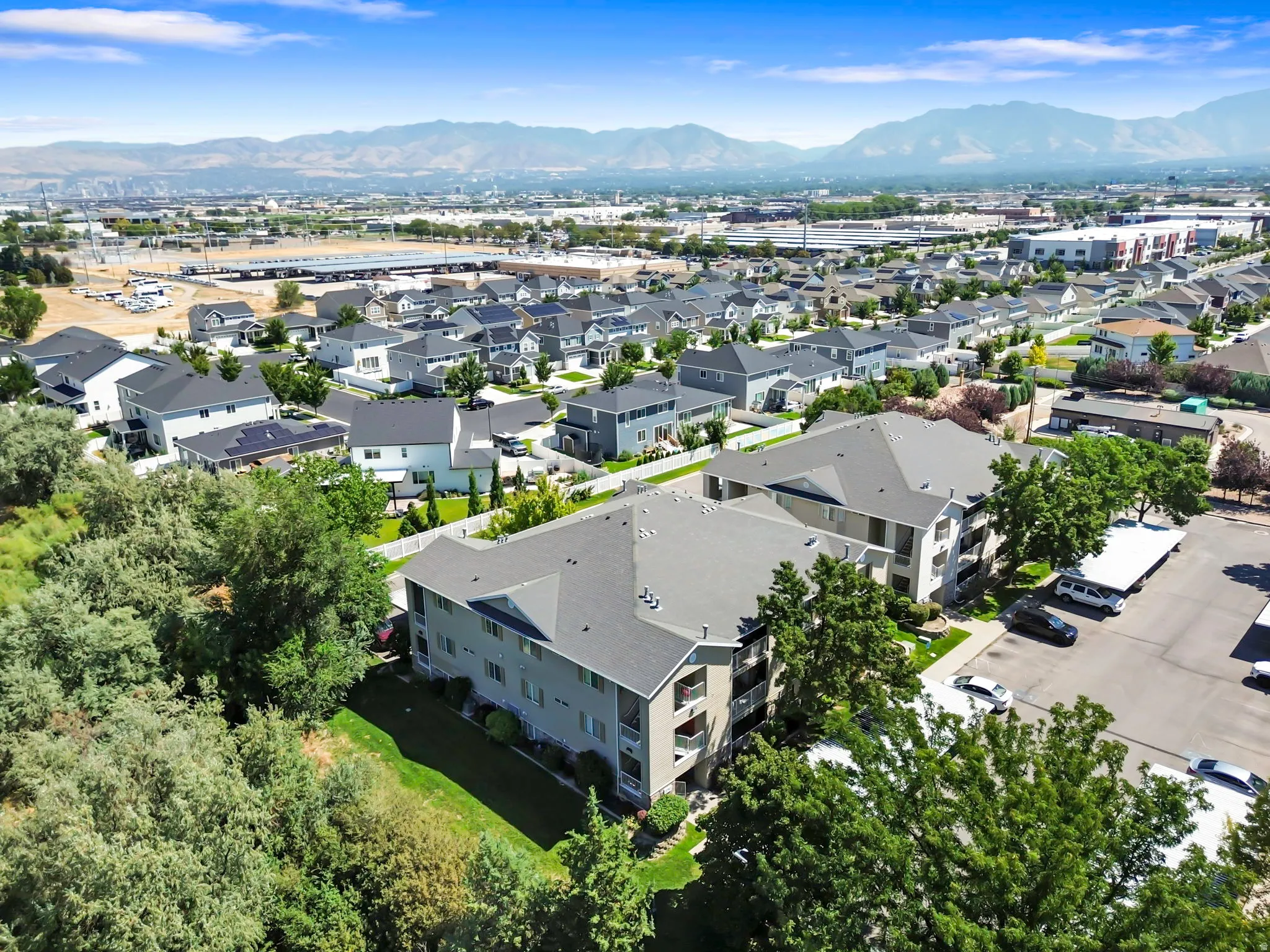 Multistory residential building with balconies, surrounded by mature trees and paved parking areas
