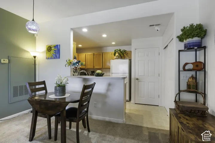 Open-concept dining space featuring textured carpeting, a stylish pendant light fixture, and a pass-through counter to the kitchen