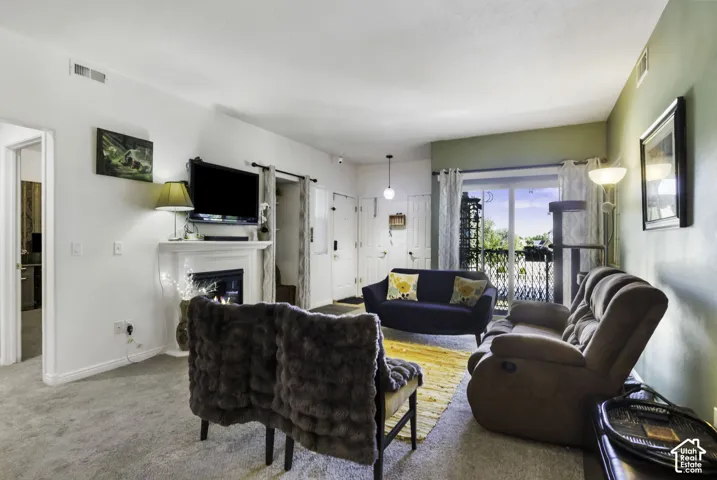 Living area featuring a fireplace with a white mantel, sliding glass doors to a balcony, and light-colored carpeting