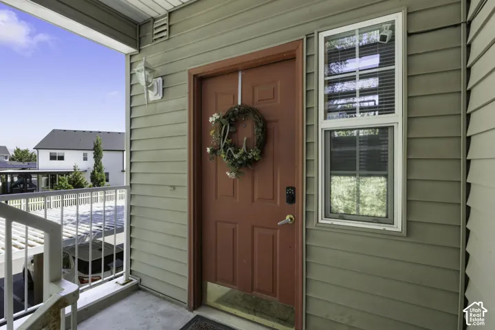 Covered entry with concrete flooring, framed by a red paneled door with smart lock hardware and a white-framed window