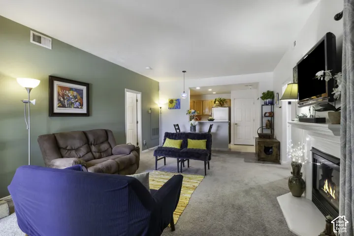 Spacious living area featuring a fireplace with a white mantel, overhead lighting, and light-colored carpeting