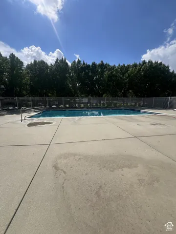 Outdoor swimming pool with concrete decking, surrounded by a perimeter fence and mature trees