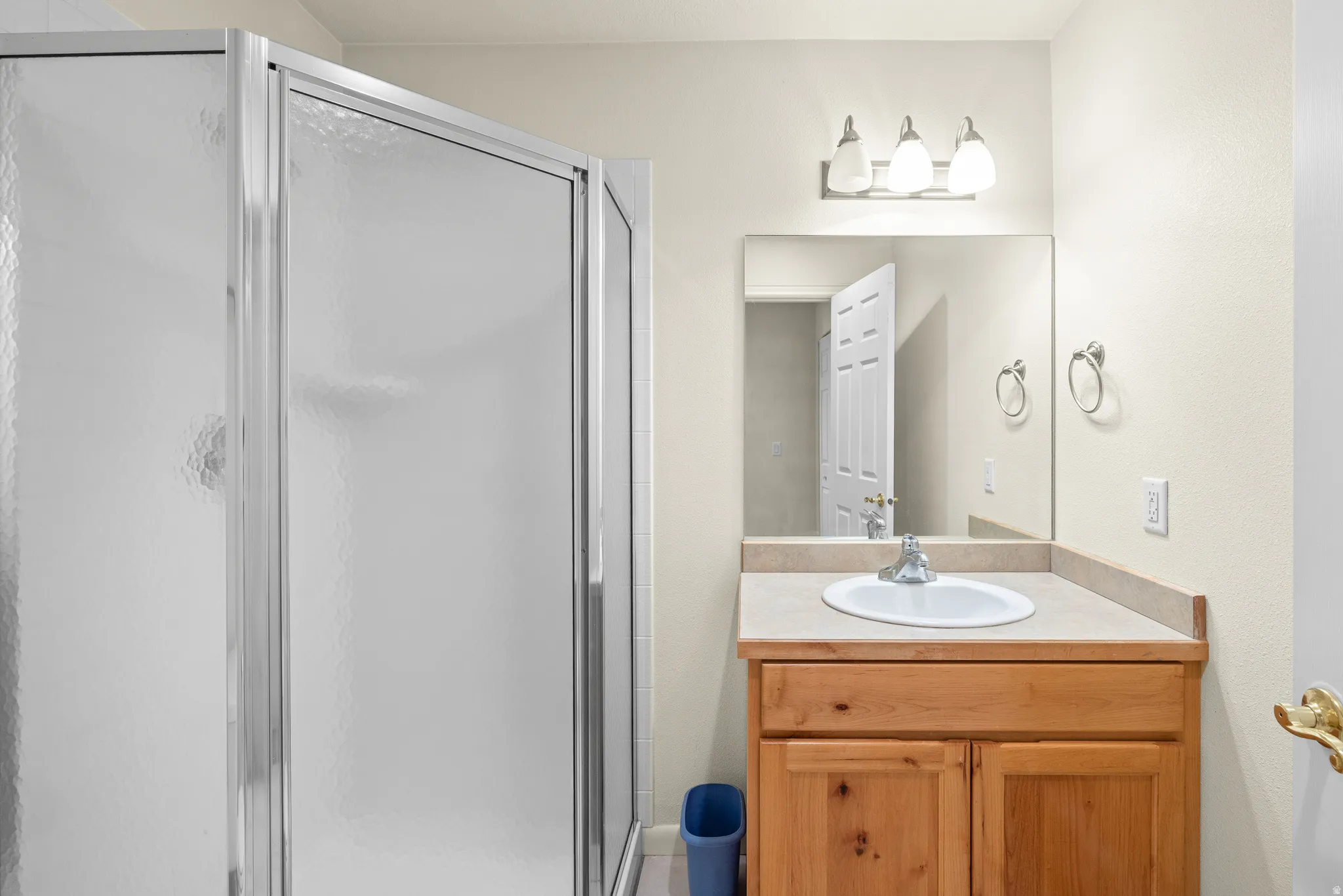 Frosted glass shower enclosure, wood-finish vanity with cabinet storage, integrated sink, and wall-mounted vanity lighting