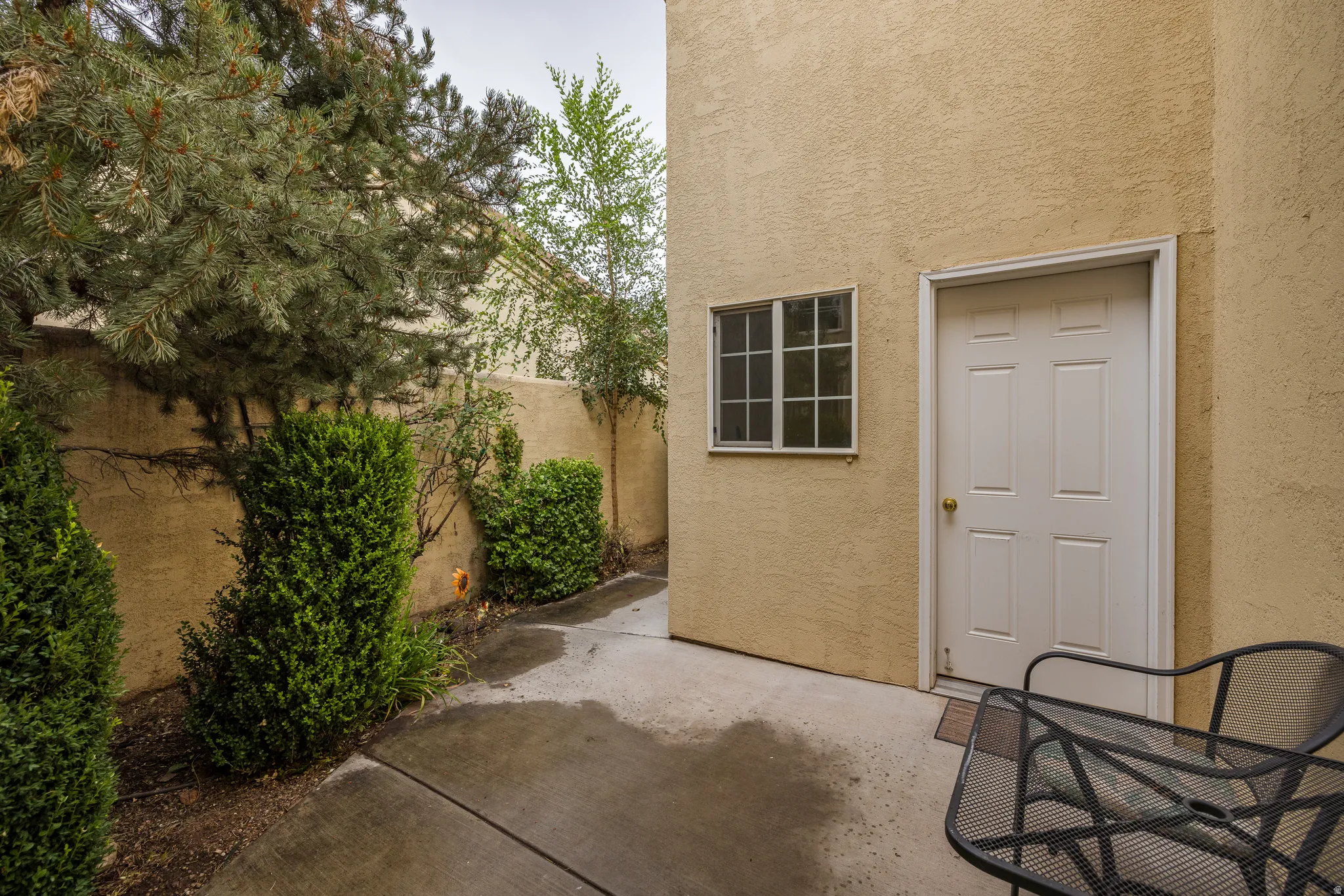 Private paved patio with stucco walls, a four-panel exterior door, and an adjacent window with grid panes