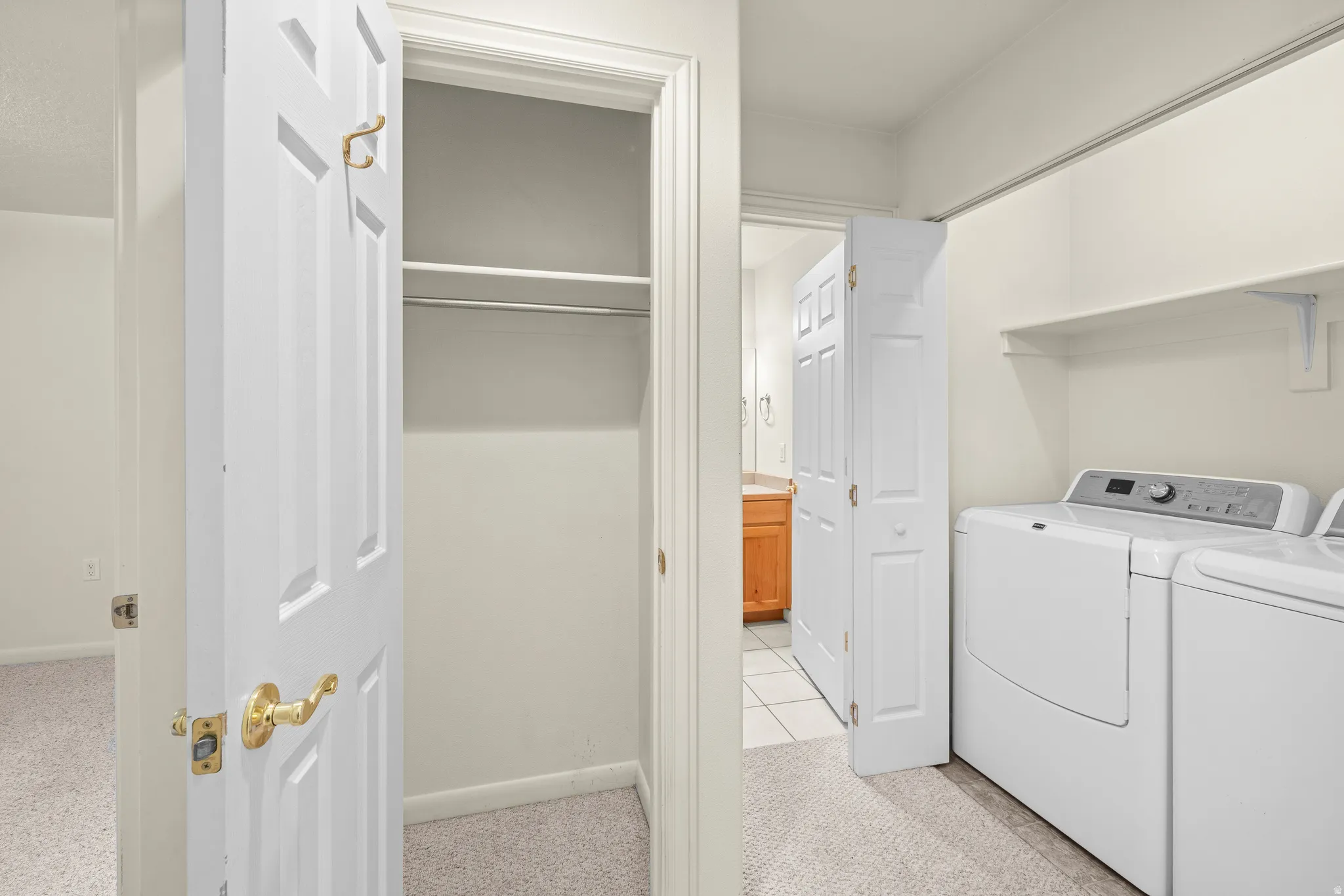Laundry area with built-in shelving, white appliances, and light-toned carpeting