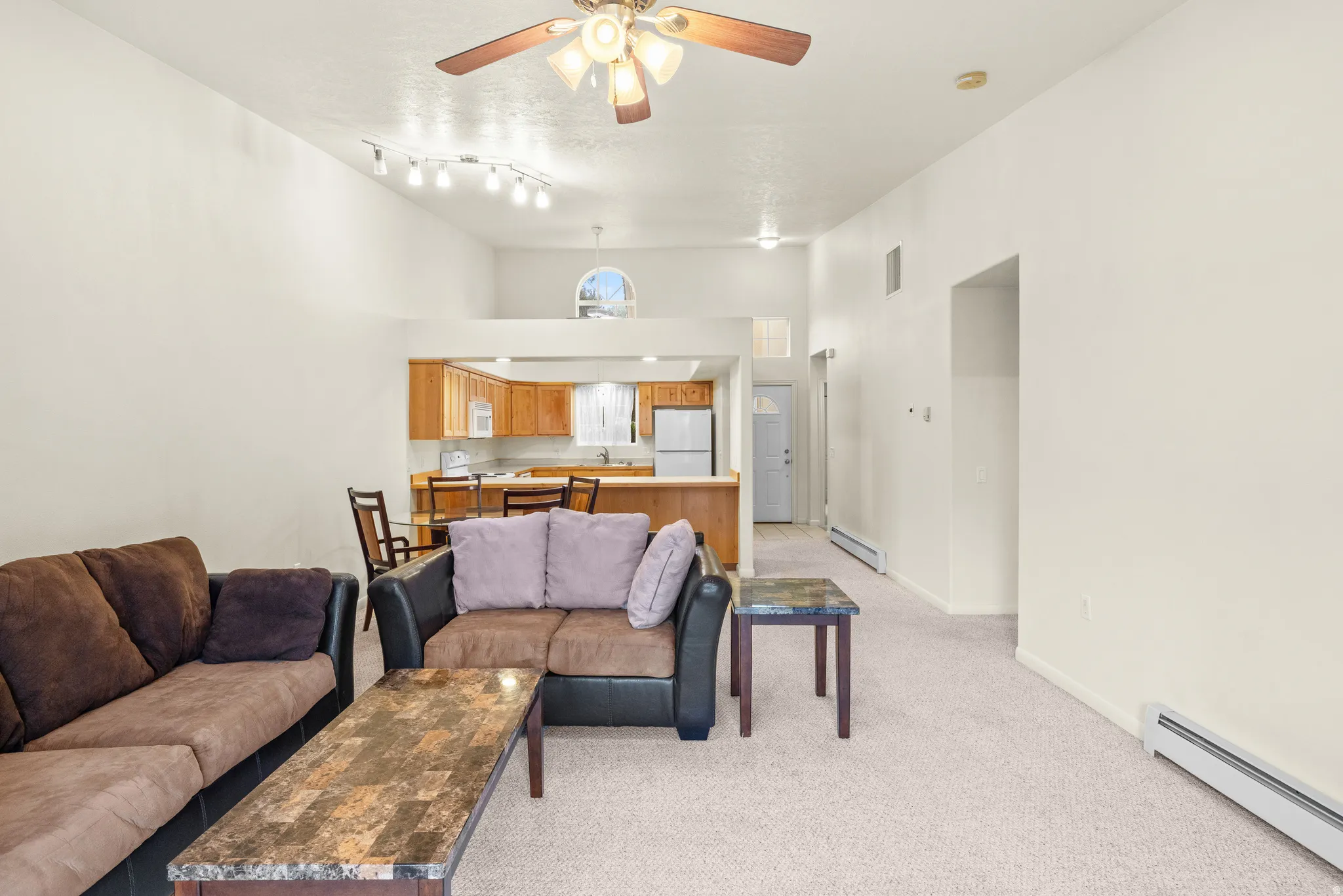 Vaulted ceilings, track lighting, ceiling fan, carpet flooring, and an arched transom window