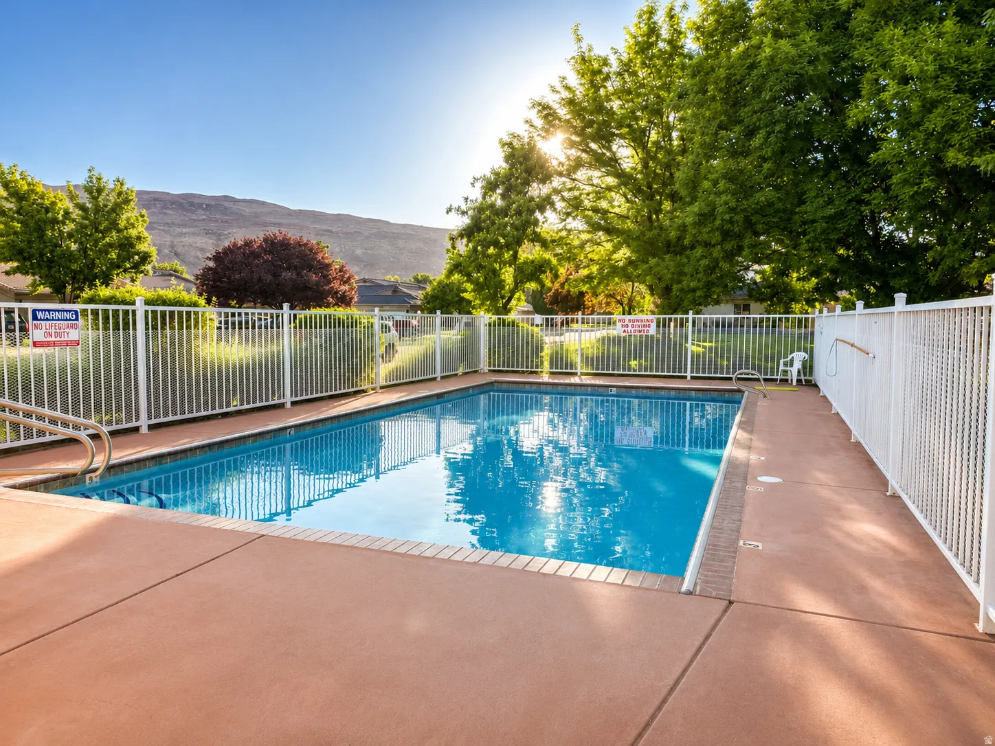 Rectangular swimming pool with a surrounding concrete deck and white perimeter fencing