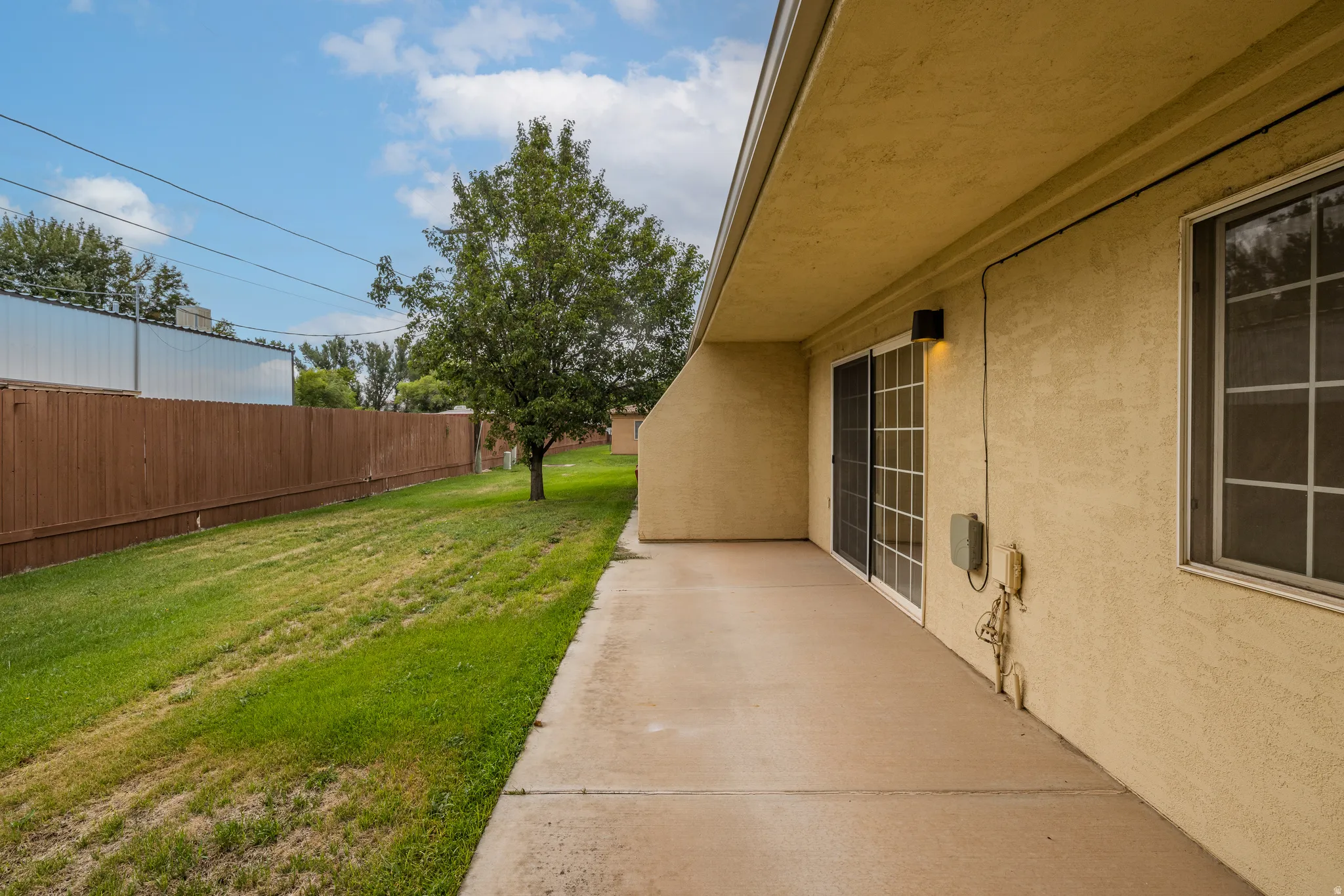 Exterior patio with a sliding glass door and an adjacent window, concrete flooring, and a stucco finish