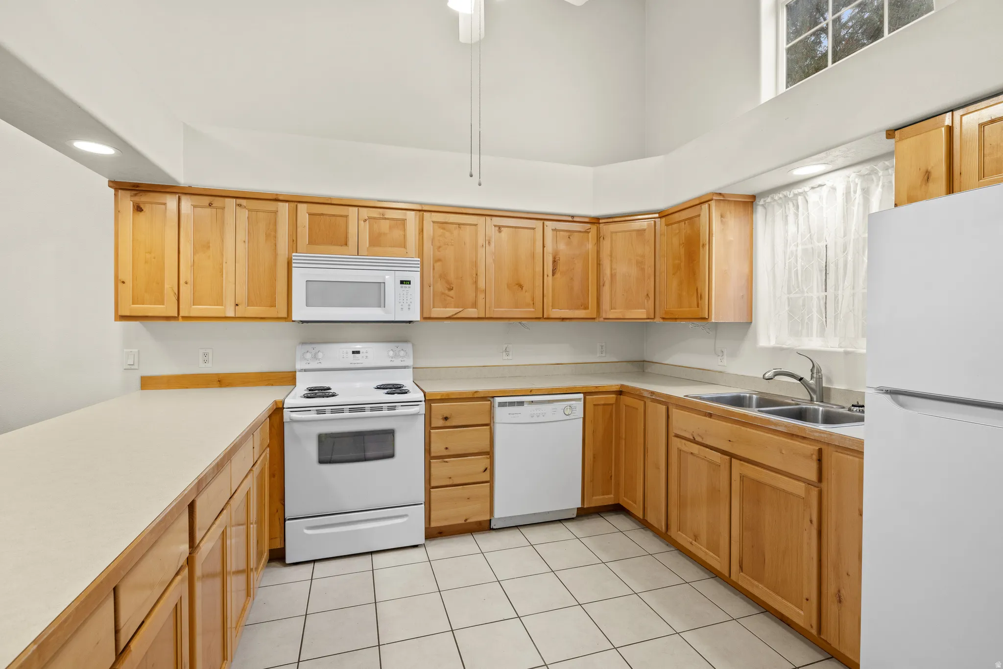 U-shaped kitchen layout with wood-finish cabinetry, neutral countertops, tile flooring, and vaulted ceiling