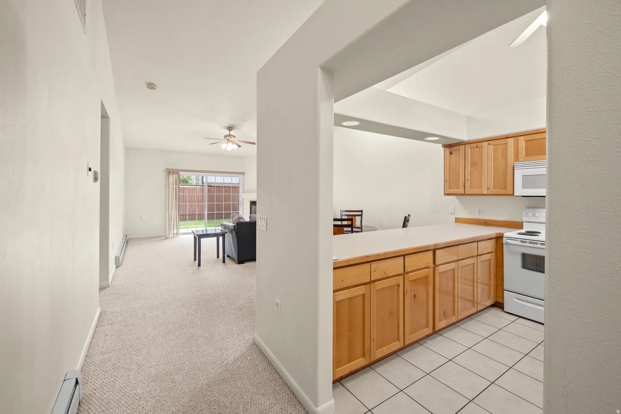 Kitchen with light wood cabinetry, white appliances, and tiled flooring