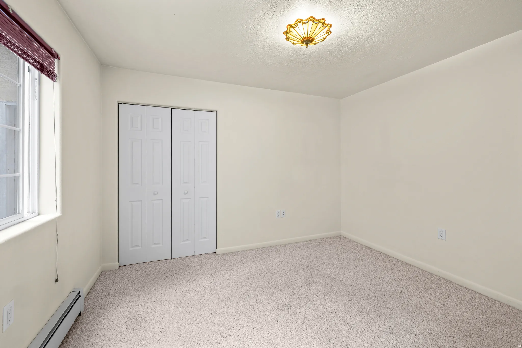 Neutral-toned carpeting, window with blinds, bi-fold closet doors, and flush-mount ceiling lighting