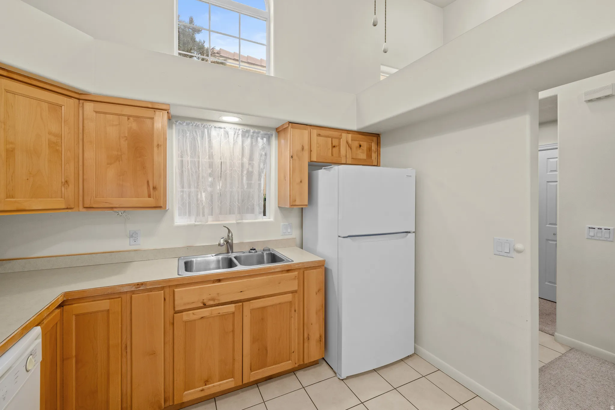 Kitchen with wood cabinetry, light-toned countertops, a double basin stainless steel sink, and tile flooring