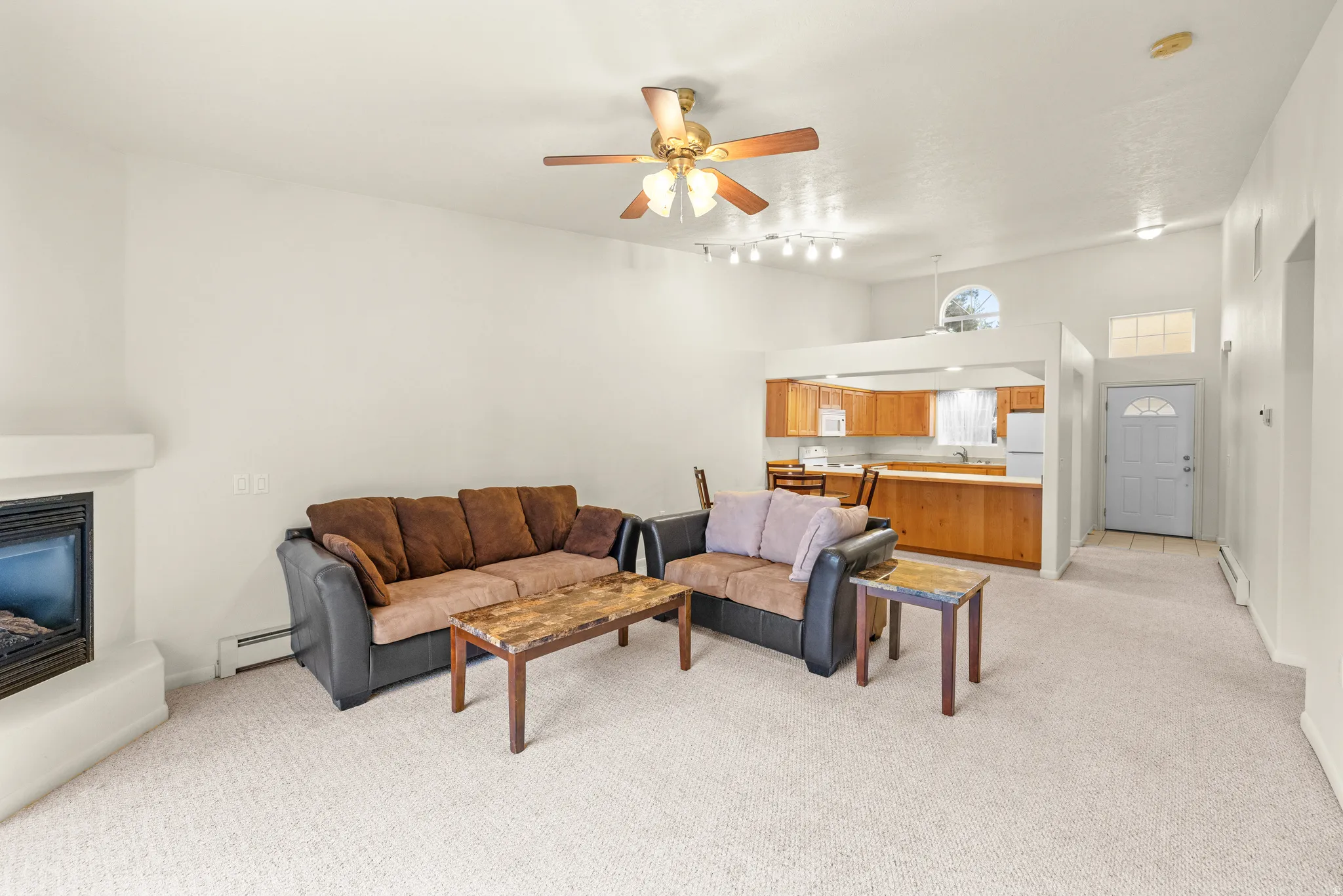 Open-concept living area featuring a fireplace, vaulted ceilings, and a ceiling fan