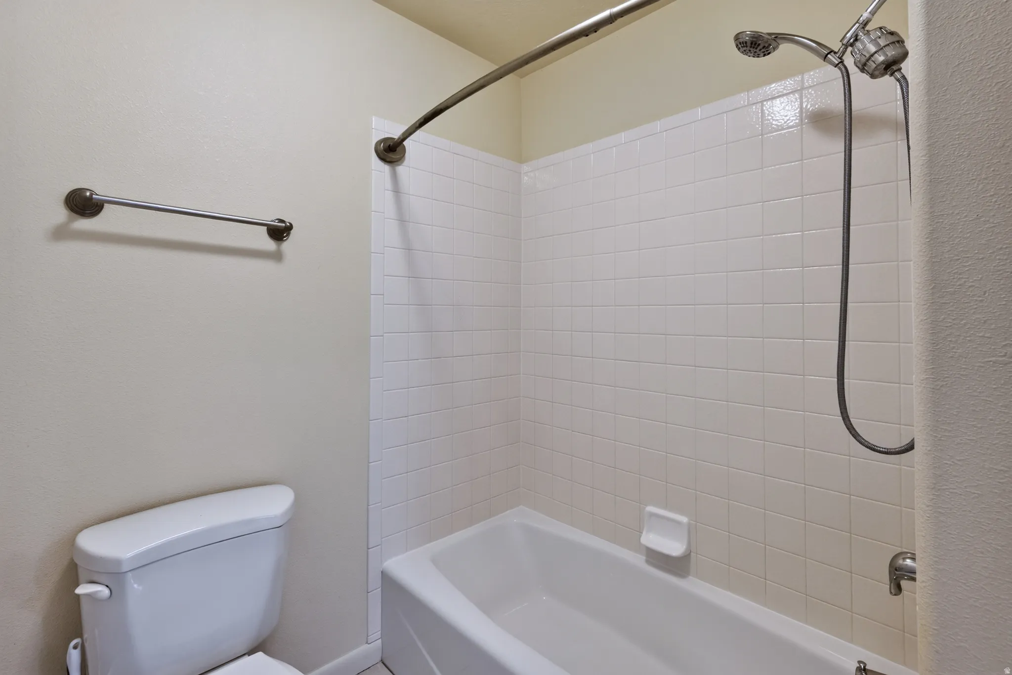 White tiled shower surround with a fixed showerhead and handheld sprayer, complete with a classic white bathtub and a curved shower rod