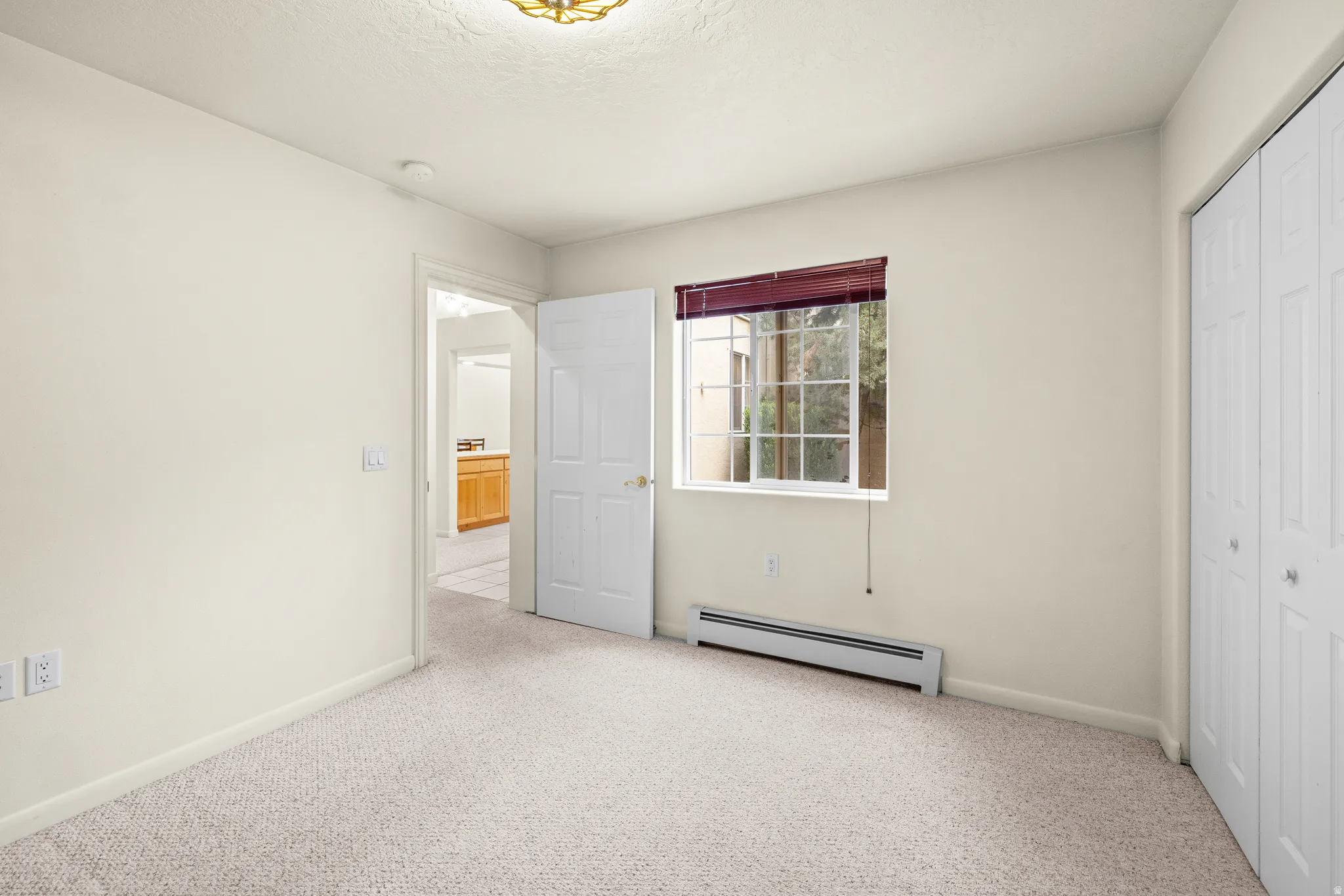 Light-toned wall paint, carpet flooring, a window with blinds, and white bi-fold closet doors