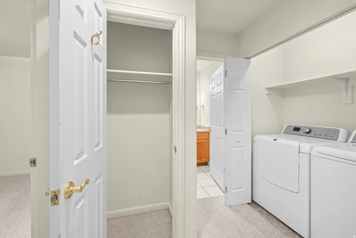 Laundry area with built-in shelving, white appliances, and light-toned carpeting