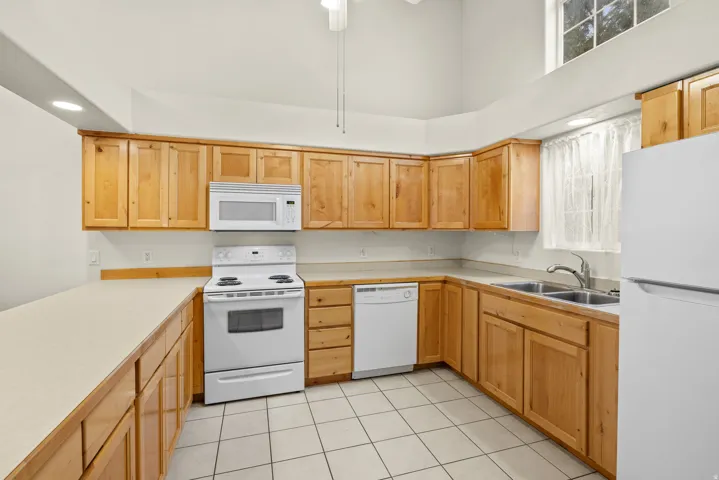 U-shaped kitchen layout with wood-finish cabinetry, neutral countertops, tile flooring, and vaulted ceiling