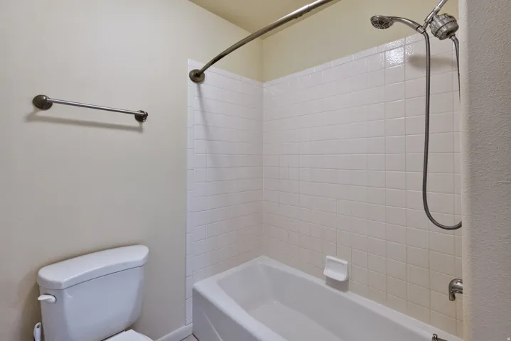 White tiled shower surround with a fixed showerhead and handheld sprayer, complete with a classic white bathtub and a curved shower rod