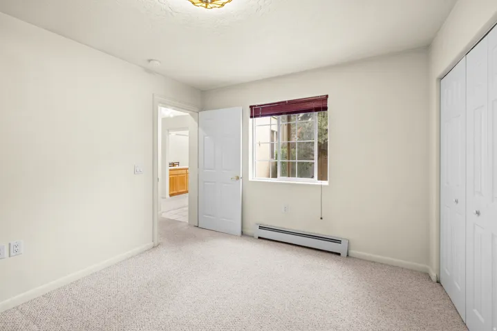 Light-toned wall paint, carpet flooring, a window with blinds, and white bi-fold closet doors