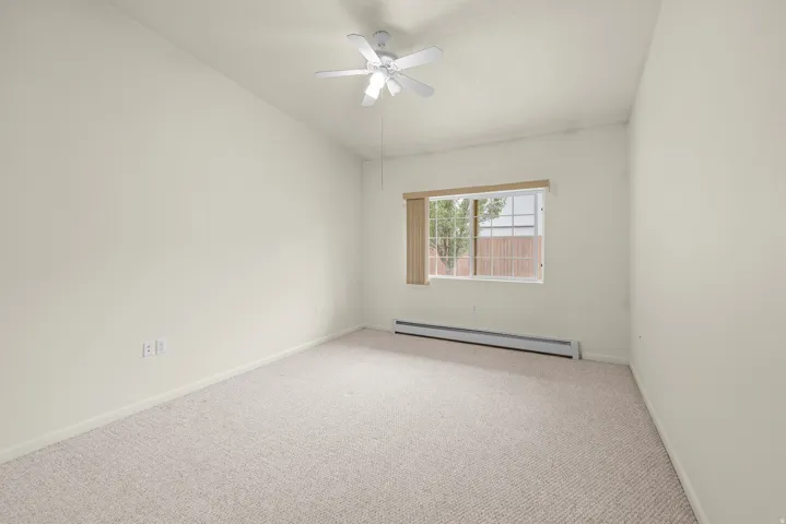 Carpeted room featuring a window with vertical blinds, a ceiling fan, and baseboard heating