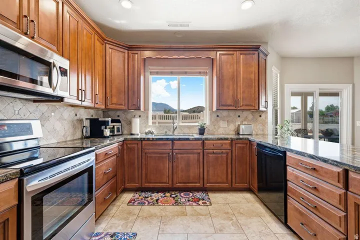 Well-appointed kitchen featuring extensive wood cabinetry, dark stone countertops, stainless steel appliances, and a tiled backsplash