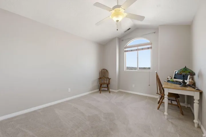 Carpeted room featuring a ceiling fan with integrated lighting, an arched window, and vaulted ceilings