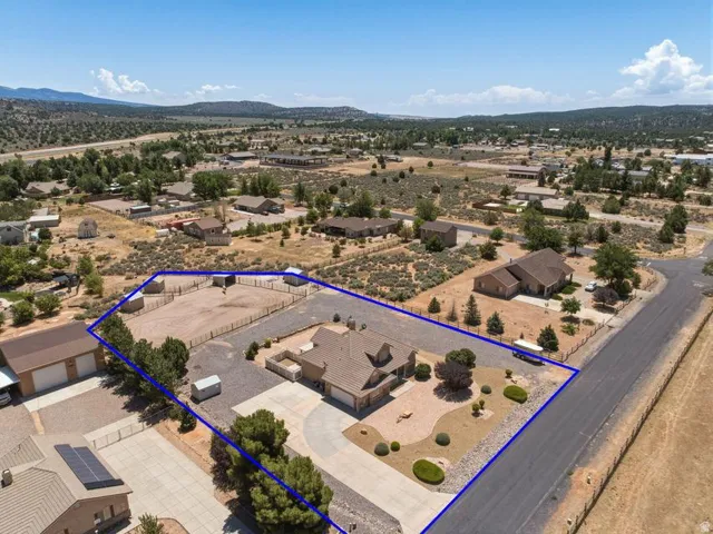 Expansive property featuring a single-story residence, separate detached garage with covered parking, circular driveway, fenced equestrian arena, and desert landscaping