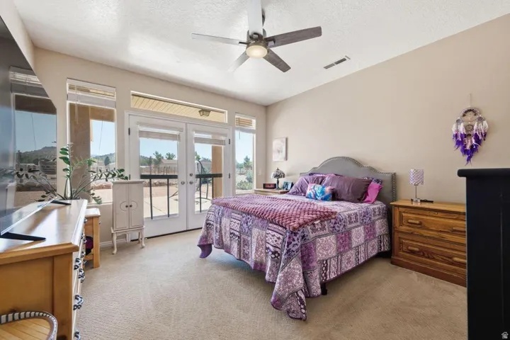 Carpeted bedroom featuring a ceiling fan with light fixture, neutral wall tones, and double French doors with sidelights