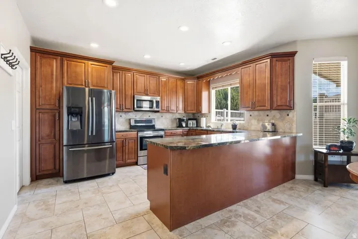 Spacious kitchen featuring extensive wood cabinetry, stainless steel appliances, durable tile flooring, and a large countertop island